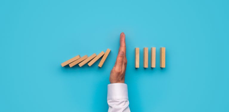 a persons hand blocking the fall of dominos halfway