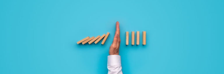 a persons hand blocking the fall of dominos halfway